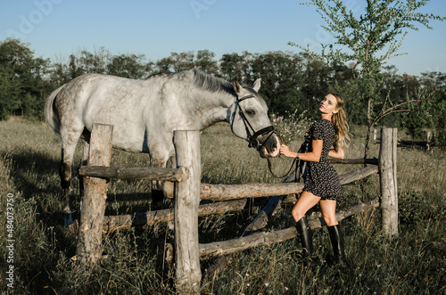 A young beautiful woman feed a white horse in a field in the summer among the grass. full-length photo. Rustic, countryside style, Love for animals concept. © Olga Kravchenko