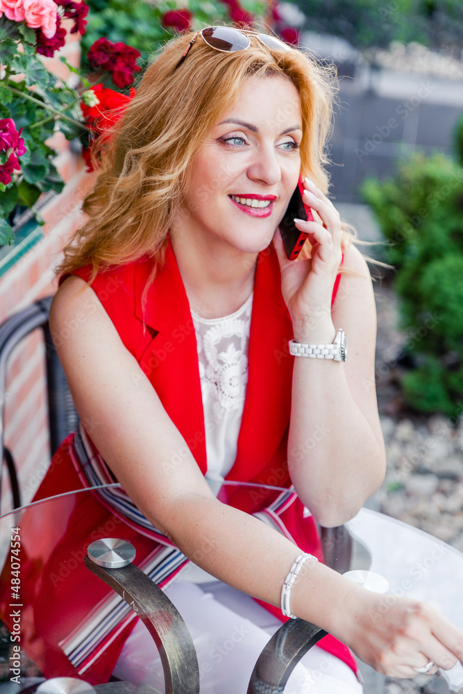 Fototapeta premium Beautiful mature woman businesswoman in white and red suit talking on the phone