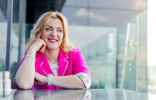 Successful woman entrepreneur in a magenta jacket posing on the terrace of a cafe in a business center.