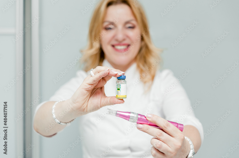 A woman doctor-cosmetologist holds in her hands a device for mesotherapy and an ampoule with a solution A woman doctor-cosmetologist holds in her hands a device for mesotherapy and an ampoule with a solution