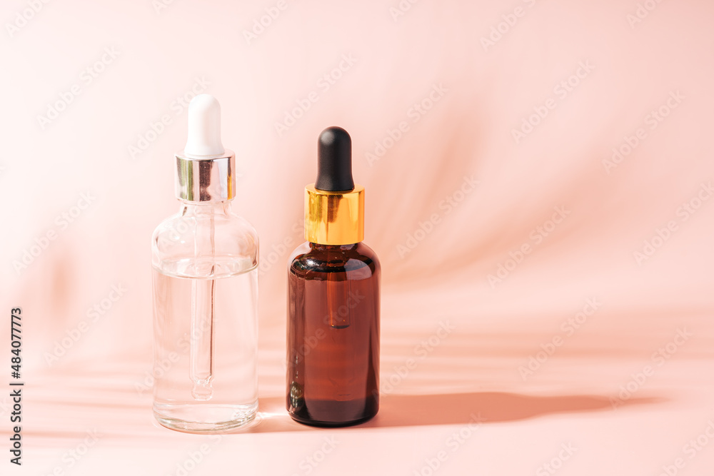 Dark and light glass bottles with pipettes on pink background.