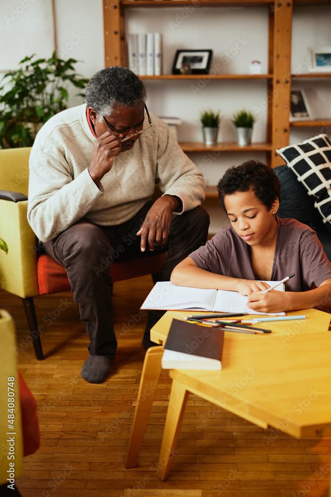An African-American grandfather is sitting at home with his grandson and helping him with homework. An African-American grandfather is sitting at home with his grandson and helping him with homework.