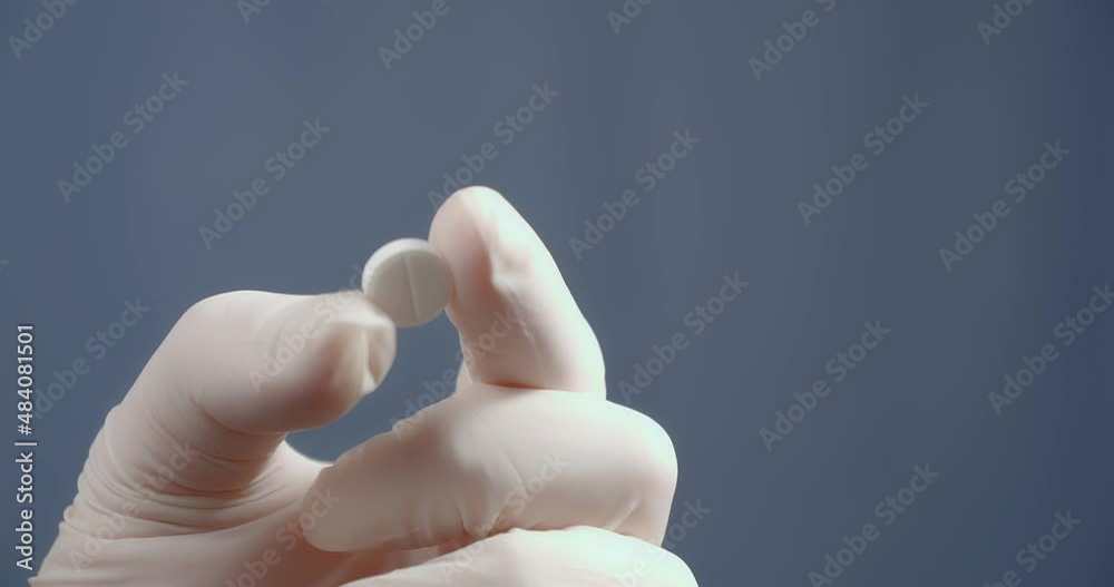 A hand in a medical glove shows a pill. A hand in a medical glove shows a pill.
