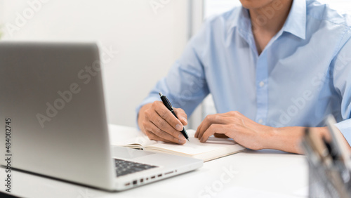 Working Man Conept The man who sits at his desk concentrating on the laptop  writing something down on the paper