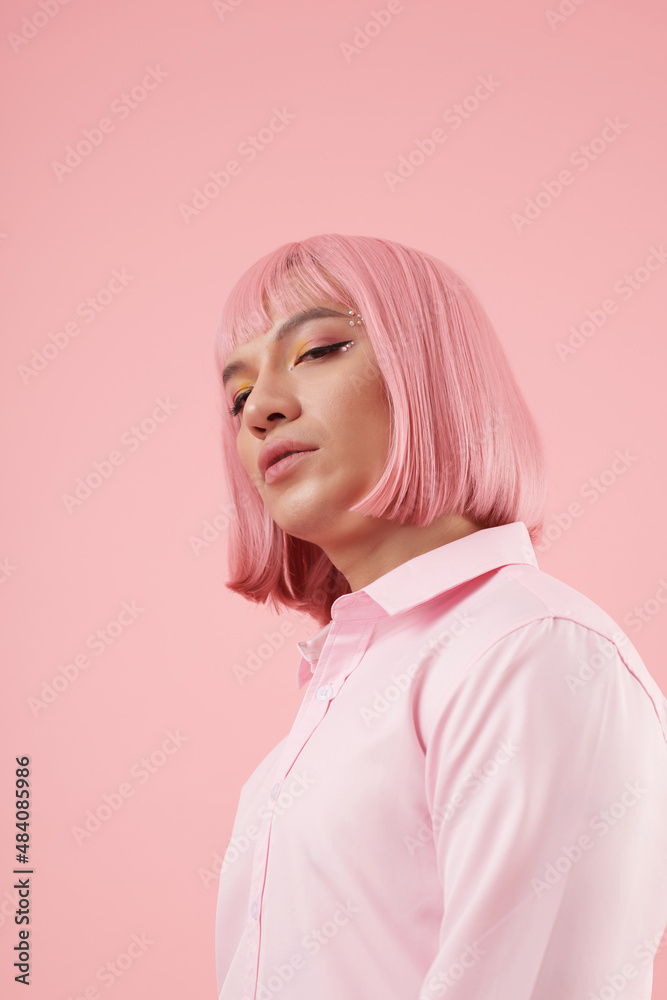 Portrait of young man with bright makeup and light pink wig looking at camera