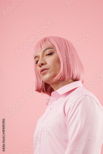 Portrait of young man with bright makeup and light pink wig looking at camera