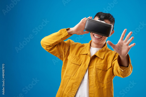 Positive young man testing new application for virtual reality headset, isolated on blue photo