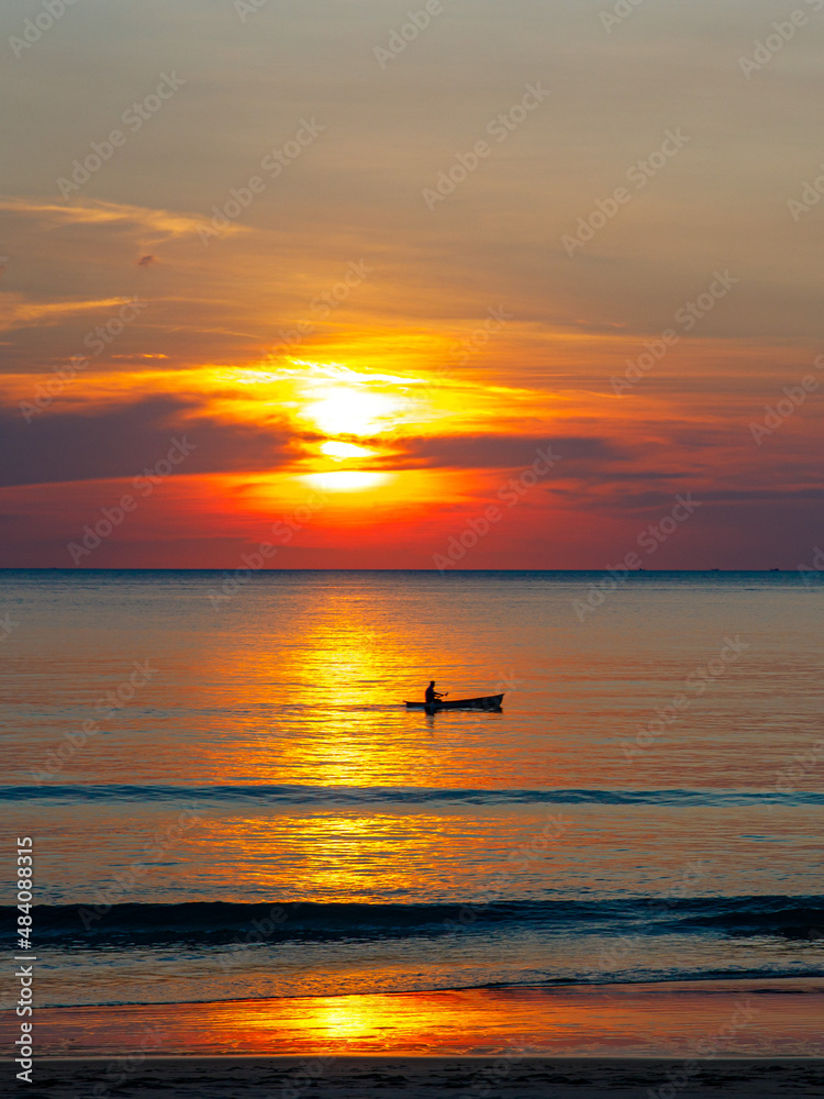 Magic sunset view seascape with beautiful colorful red orange blue sky, sun and clouds. Fisherman boat on solar path with white foam of ocean. Karon Beach Phuket Thailand. Selective focus, vertical