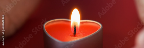 Female hands holding a heart shaped candle in dark closeup