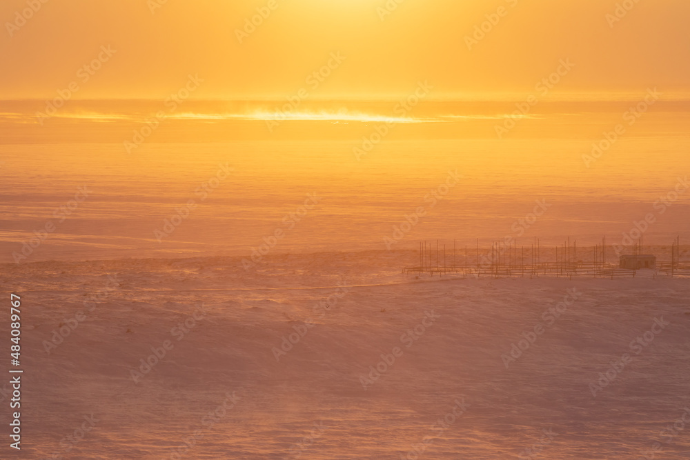 Winter arctic landscape. Morning aerial view of the snowy tundra. A frozen sea in the distance. Beautiful golden light at sunrise. Cold windy and frosty weather. Chukotka, Siberia, Far North of Russia