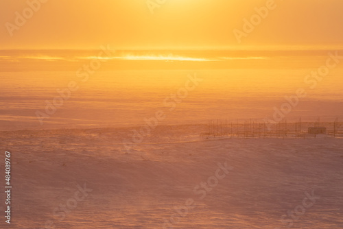 Winter arctic landscape. Morning aerial view of the snowy tundra. A frozen sea in the distance. Beautiful golden light at sunrise. Cold windy and frosty weather. Chukotka, Siberia, Far North of Russia