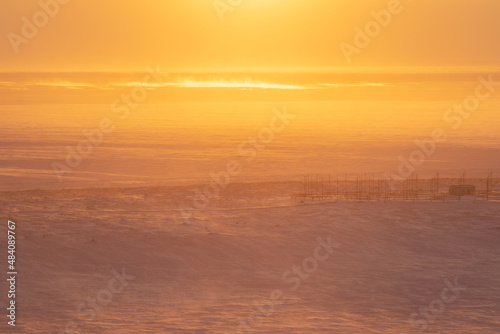 Winter arctic landscape. Morning aerial view of the snowy tundra. A frozen sea in the distance. Beautiful golden light at sunrise. Cold windy and frosty weather. Chukotka, Siberia, Far North of Russia