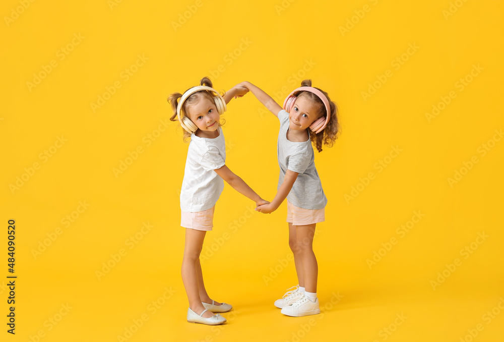 Fototapeta premium Cute little girls in headphones holding hands on yellow background