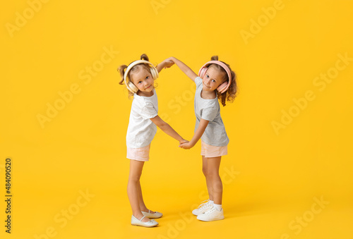 Cute little girls in headphones holding hands on yellow background