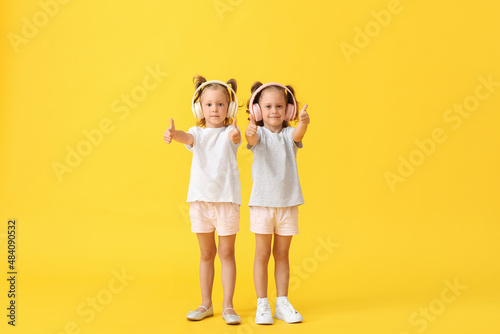 Cute little girls in headphones showing thumbs-up on yellow background © Pixel-Shot