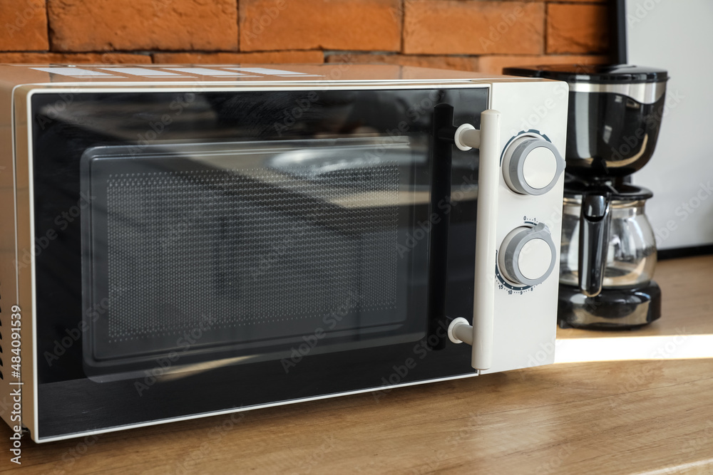 Modern microwave oven on wooden counter near brick wall Modern microwave oven on wooden counter near brick wall