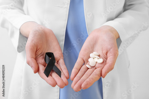 Woman with black ribbon and pills on light background, closeup. Melanoma concept