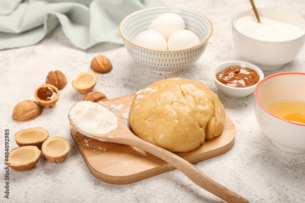 Wooden board of fresh dough for preparing walnut shaped cookies with boiled condensed milk and ingredients on light background Wooden board of fresh dough for preparing walnut shaped cookies with boiled condensed milk and ingredients on light background