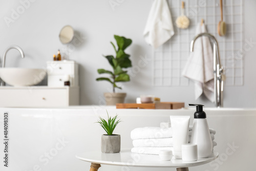 Set of cosmetic products  towels and plant on table in bathroom