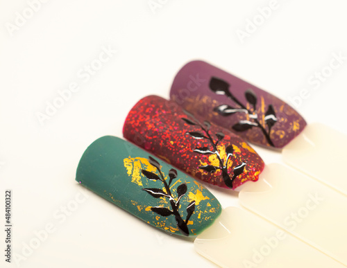 Glittery nail designs. Colorful matte gel polish with golden aluminium foil decorations and black painted plant branches. Selective focus on the details, object isolated on white background.