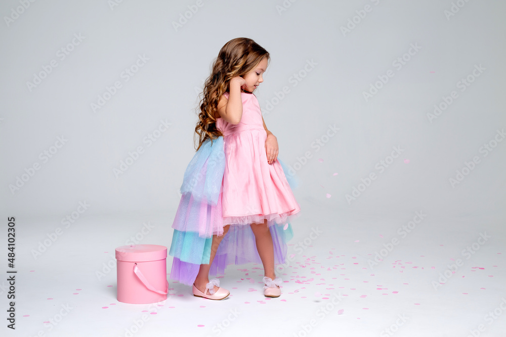 beautiful little girl in a chic pink dress poses standing on a gray ...