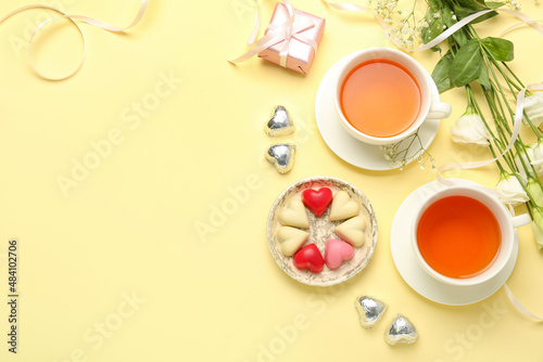 Composition with tasty heart-shaped candies, flowers and cups of tea for Valentine's Day celebration on beige background