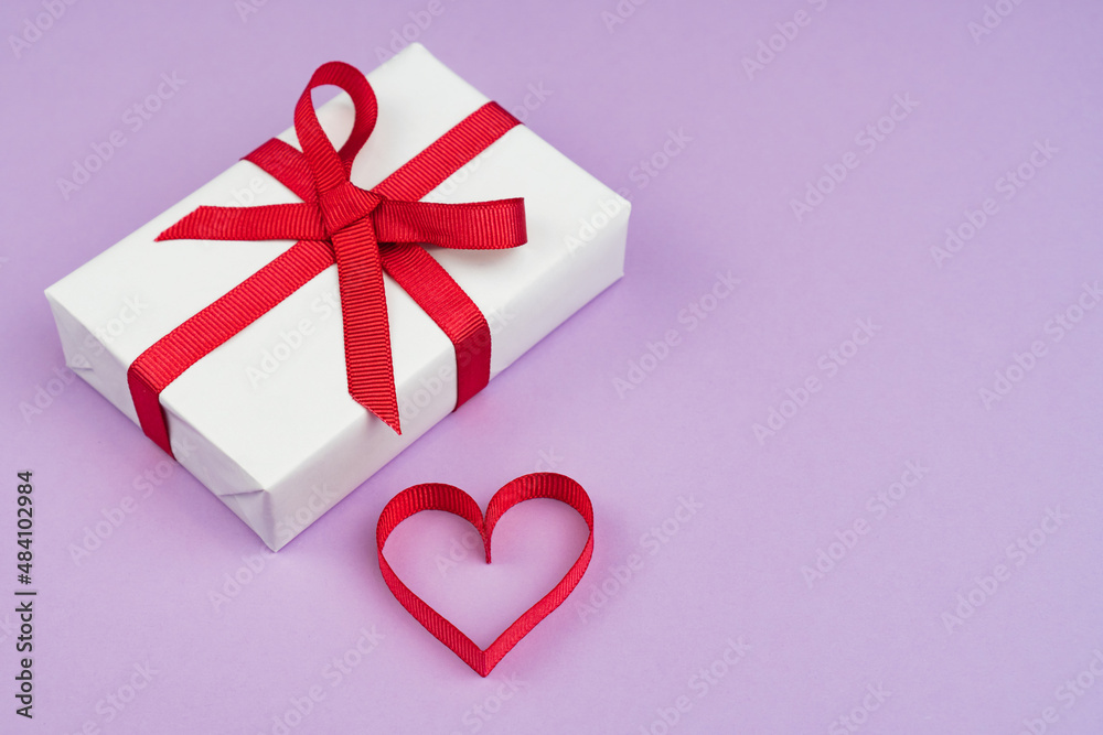Valentine's Day or birthday concept with copy space. Red ribbon heart and gift box on purple papper Valentine's Day or birthday concept with copy space. Red ribbon heart and gift box on purple papper