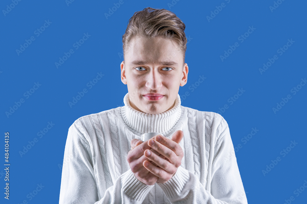 Cold winter. A man is holding a cup with a drink. Not enough warmth. The blond gets warm from the cold with hot coffee or tea. Cool indoors. It's winter time. Dress warmly Cold winter. A man is holding a cup with a drink. Not enough warmth. The blond gets warm from the cold with hot coffee or tea. Cool indoors. It's winter time. Dress warmly
