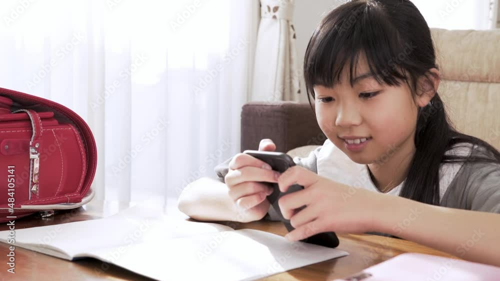 勉強中にスマホを見る小学生の女の子 勉強中にスマホを見る小学生の女の子