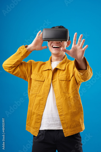 Happy millennial man in vr glasses playing and trying to touch something when exploring simulation of world photo