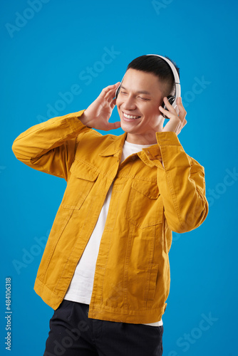Portrait of happy young man enjoying good music in his headphones and dancing photo