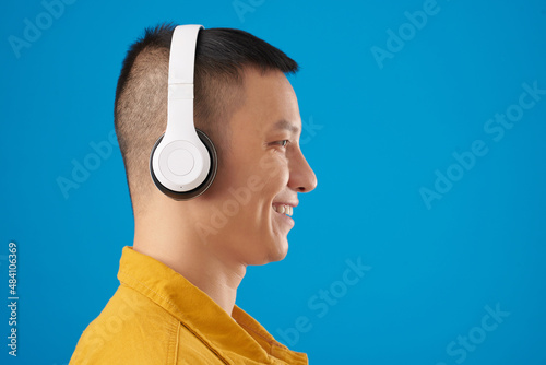 Side view of smiling young man in headphones listening to music, audiobook or podcast photo