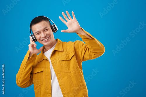 Joyful young man in headphones listening to music and waving with hand photo