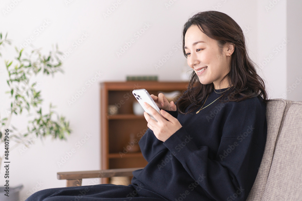 ソファーに座りながらスマホを見ているアジア人女性、自宅リビング ソファーに座りながらスマホを見ているアジア人女性、自宅リビング