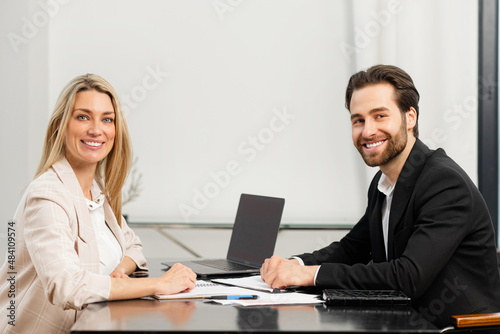 Young caucasian coworkers working out business strategy together and discuss tasks while sitting at the office desk and looking at the camera. Team work concept
