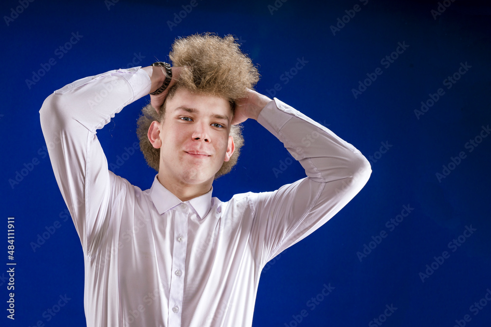 A man with curly hair holds his head with his hands on a blue background.