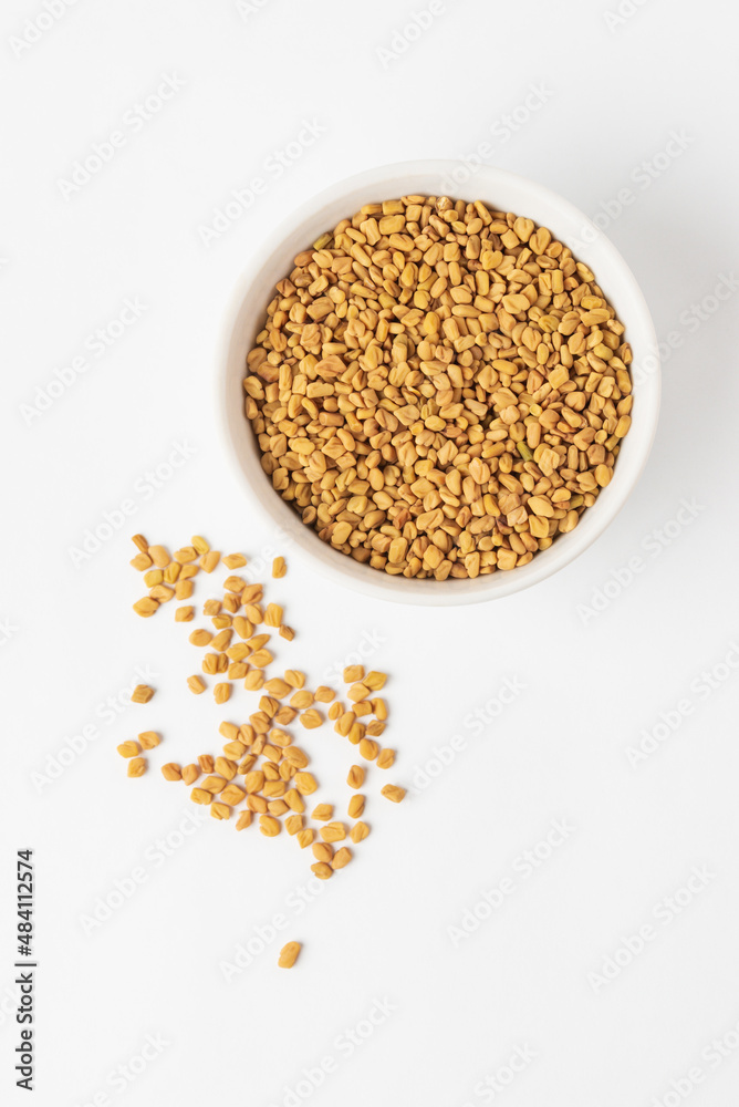 Scattered yellow fenugreek seeds or shambhala, helba seeds on white background, top view. Fenugreek is ingredient of traditional Indian cuisine Scattered yellow fenugreek seeds or shambhala, helba seeds on white background, top view. Fenugreek is ingredient of traditional Indian cuisine