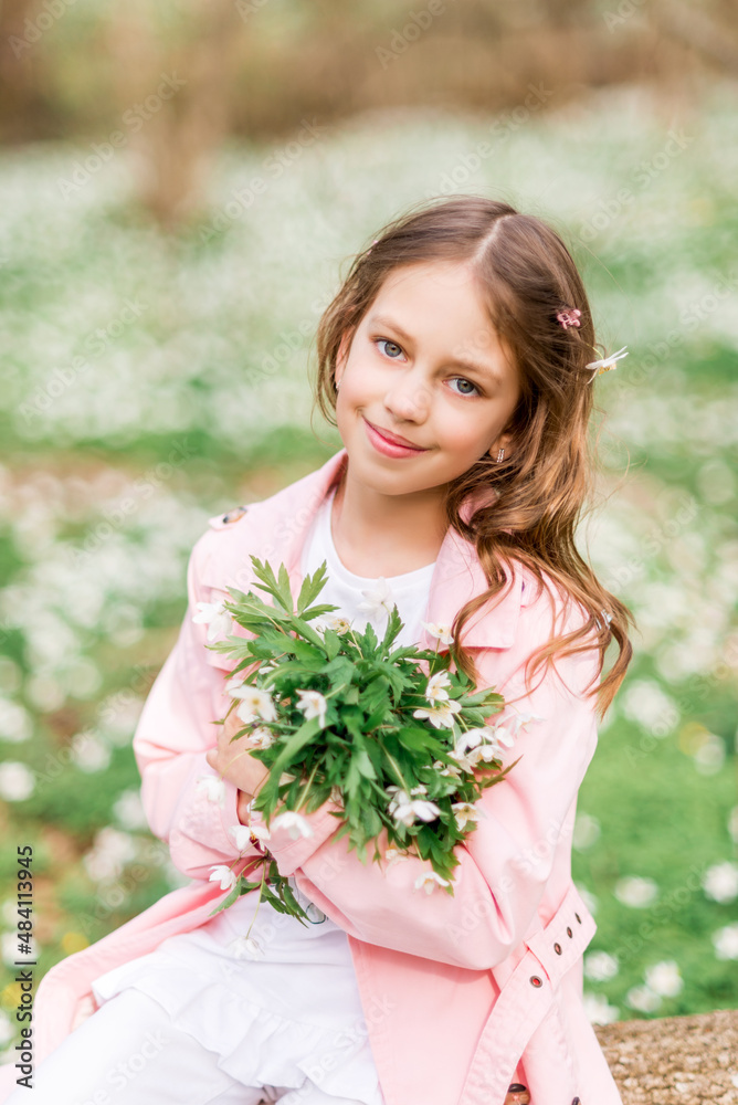 Fototapeta premium Portrait of a girl with a bouquet of anemone. A child in the spring forest.