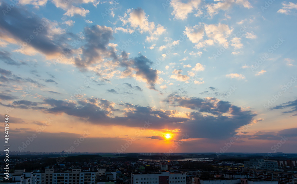 Beautiful sunset sky over the city. The sun over city houses. Bird's-eye. Blue sky and yellow clouds. Wide panorama.