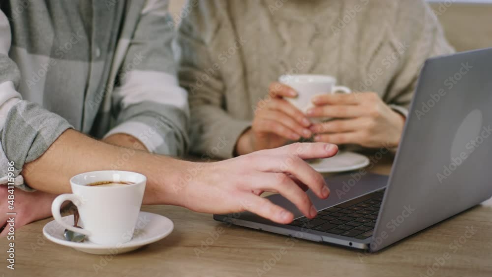 Closeup to the camera two people gesticulating with hands on the laptop while drinking the coffee at coffee shop Closeup to the camera two people gesticulating with hands on the laptop while drinking the coffee at coffee shop