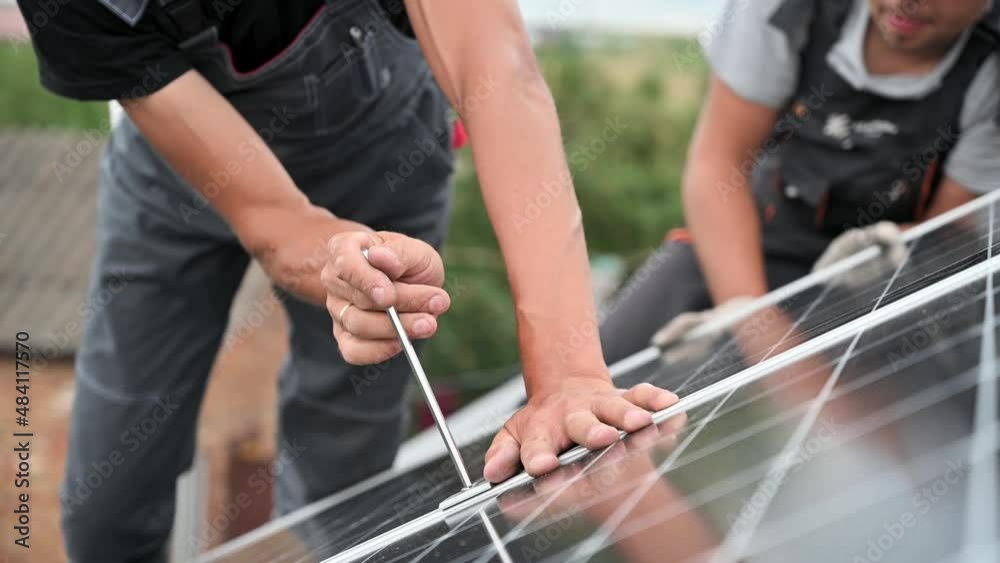 Man worker mounting photovoltaic solar moduls on roof of house. Close up of electrician installing solar panel system outdoors, tightening clamp with hex key. Concept of alternative, renewable energy.