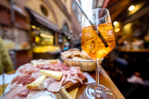 Meat plate with sliced italian sausages, proscutto, cheese, bread and Spritz Aperol drink on a table at outdoor bar on crowded street background