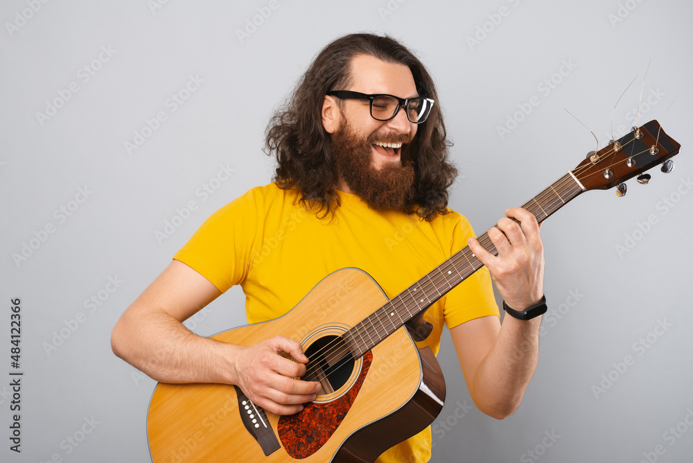 Obraz premium Cheerful young man playing at acoustic guitar and smiling.