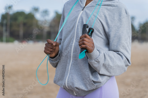 Detail of hands holding a skipping rope falling from the neck. Unrecognizable woman resting from exercise. © Marc