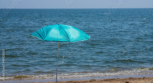 Beach umbrella with pale pink stripes in the foreground, against the blue sea background © Oleh Marchak