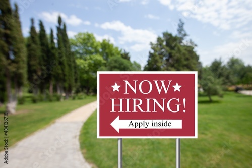 Outdoor lawn sign now hiring apply inside with a direction arrow. Employment, understaffed business photo
