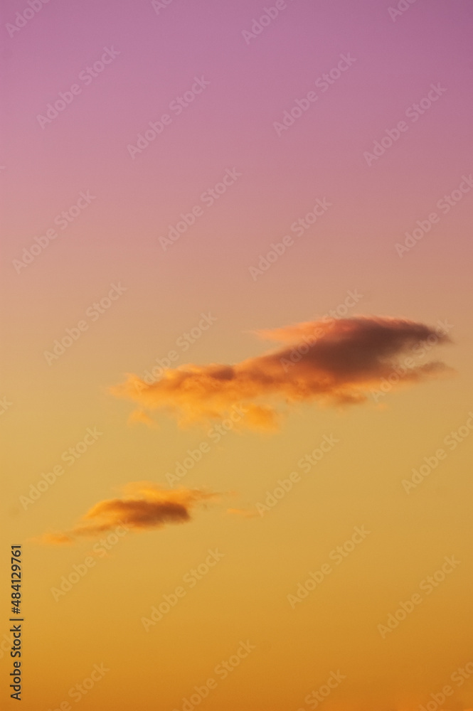 Two lone clouds on evening orange to purple gradient colored sky