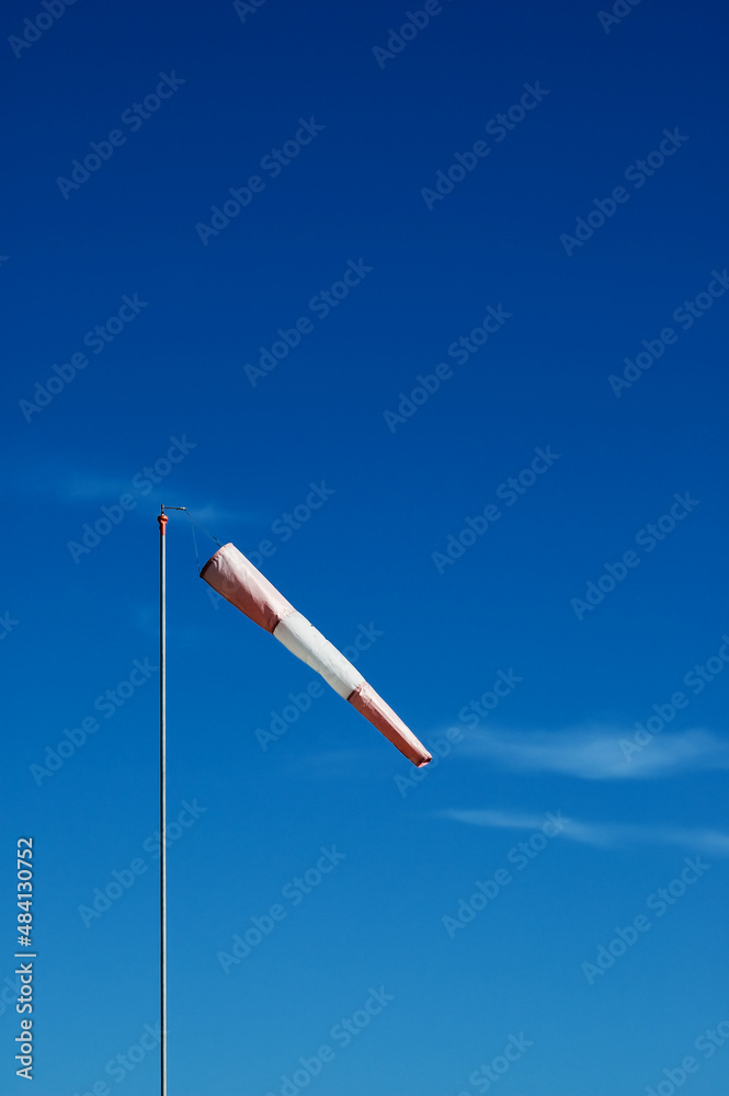 Naklejka premium Red and white windsock on a metal pole on blue sky background with cirrus clouds