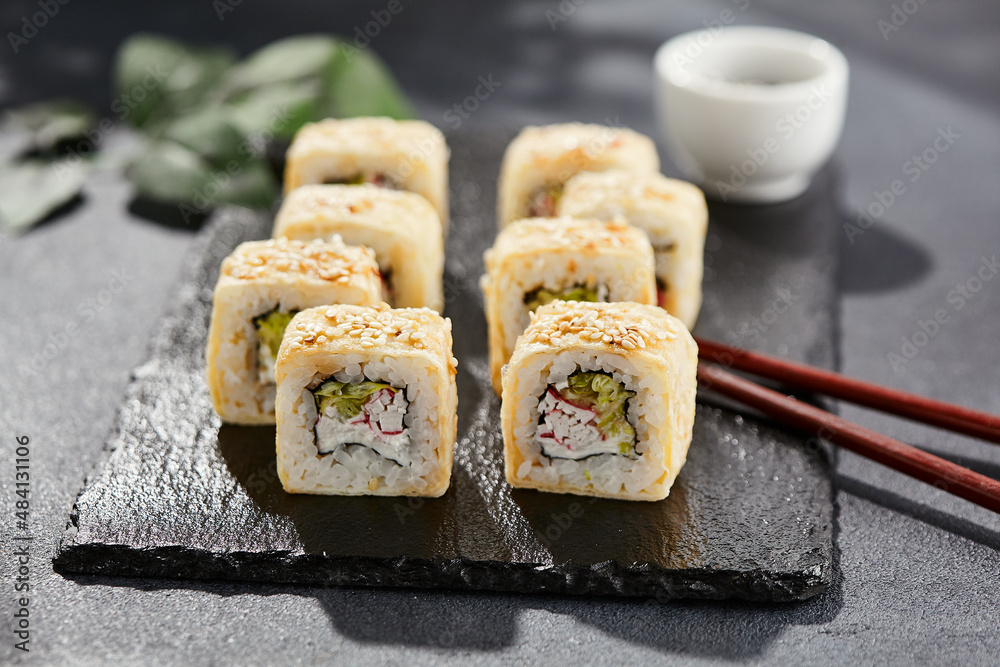 Maki sushi on dark stone table. Sushi roll crab, cheese, cucumber inside and tamago outside. Style concept japanese menu with black background, leaves and hard shadow. Maki sushi on dark stone table. Sushi roll crab, cheese, cucumber inside and tamago outside. Style concept japanese menu with black background, leaves and hard shadow.