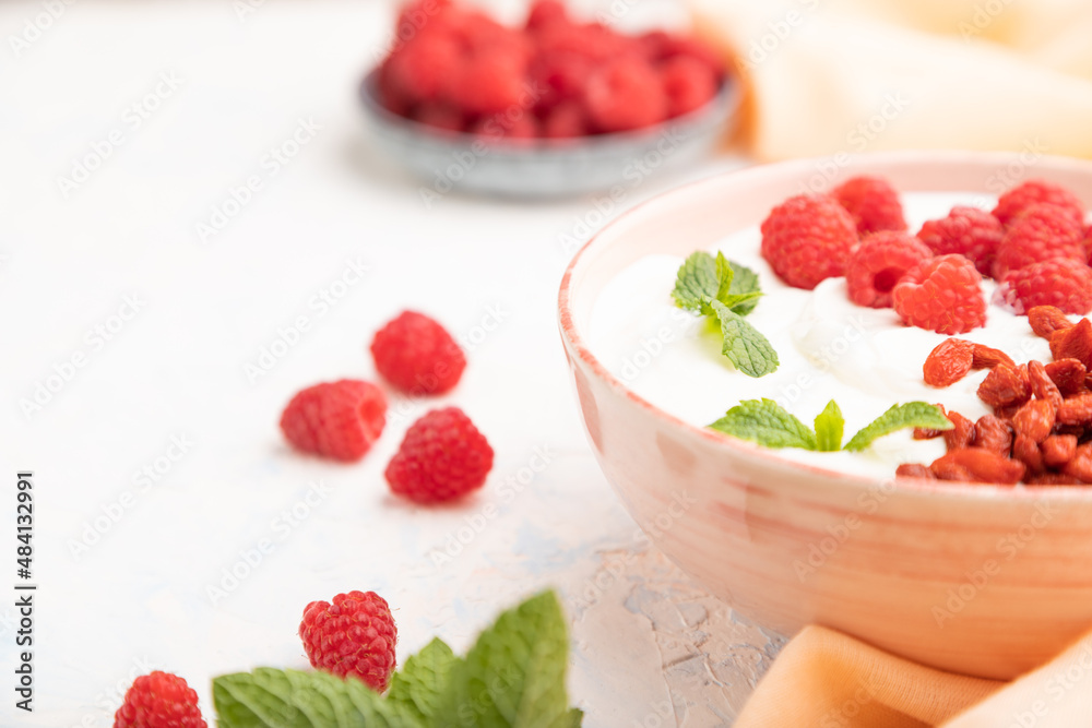 Yogurt with raspberry and goji berries in ceramic bowl on white concrete background. Side view, selective focus. Yogurt with raspberry and goji berries in ceramic bowl on white concrete background. Side view, selective focus.